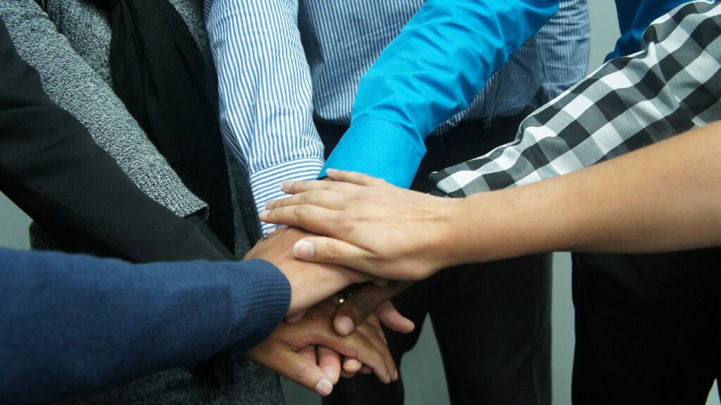 Six people each holding his or her right arm out so that each right hand touches