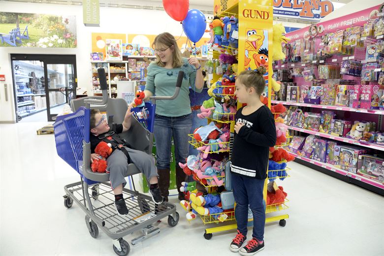 A child in a shopping cart especially designed for children with a physical disability, with his mother and sister by his side