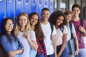 Seven teens standing in front of blue school lockers looking at camera and smiling