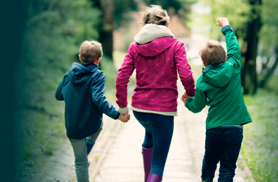 two children and parent walk down sidewalk