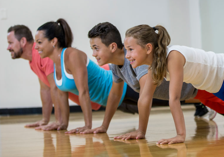 2 parents and 2 school aged children doing planks on the ground together and smiling