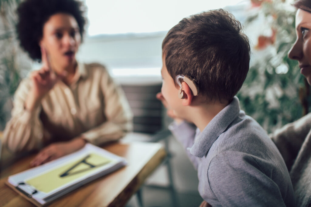 Child with a hearing aid practicing sign language with an instructor