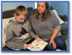 young boy reading a decodable book with his mother listening and supporting him