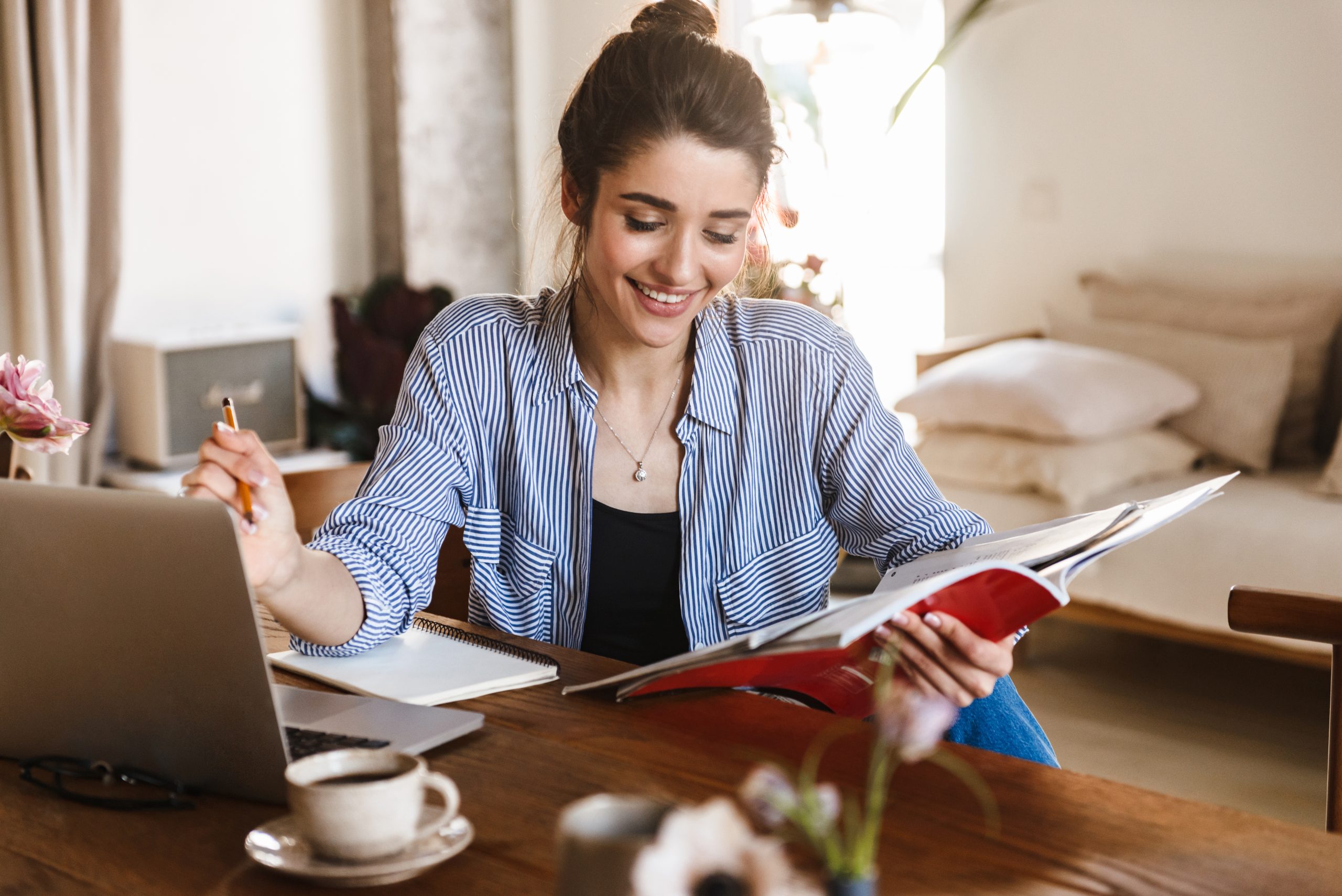 Caucasian woman studying with textbooks and using laptop at home.